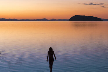 Silhouette einer Frau, die bei Sonnenuntergang am Meer steht - CAVF27667