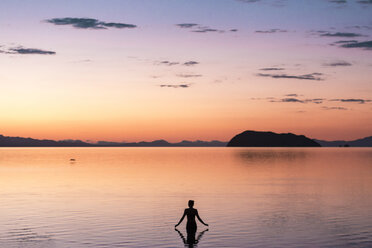 Rear view of woman standing in sea during sunset - CAVF27668