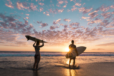 Rear view of couple with surfboards standing on shore during sunset - CAVF27693