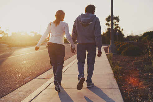 Rear view of couple walking on sidewalk on sunny day - CAVF27701