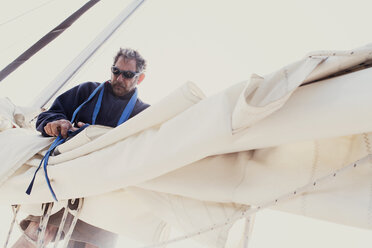 Low angle view of man tying sails of boat against clear sky - CAVF27702