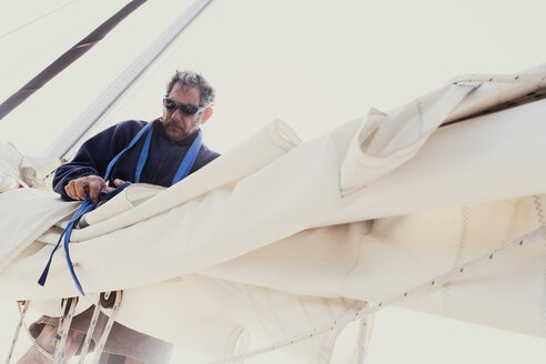 Niedriger Blickwinkel des Mannes, der die Segel des Bootes gegen den klaren Himmel bindet - CAVF27702