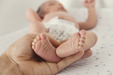 Cropped image of person holding baby's feet on bed - CAVF27703