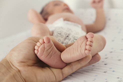 Ausgeschnittenes Bild einer Person, die die Füße eines Babys im Bett hält - CAVF27703