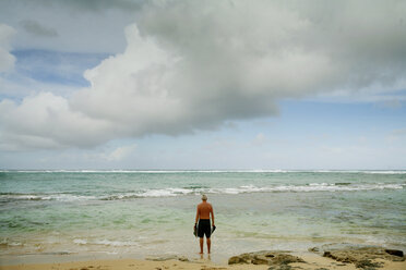 Rear view of man standing on seashore against cloudy sky - CAVF27710