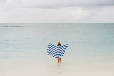 Rückansicht eines Mädchens, das ein Handtuch hält und gegen einen bewölkten Himmel zum Meer läuft - CAVF27724