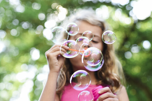 Low angle view of girl blowing bubbles at park - CAVF27740