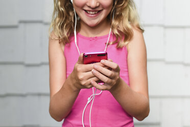 Midsection of happy girl listening music while using smart phone against wall - CAVF27741