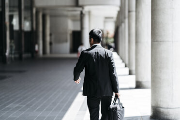 Rear view of businessman carrying briefcase while walking at colonnade - CAVF27745