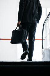 Tiefschnitt-Rückansicht eines Geschäftsmannes, der eine Aktentasche trägt, während er auf einer Rolltreppe geht - CAVF27748
