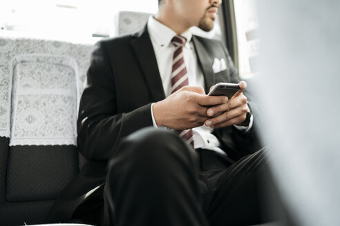 Mittelteil eines Geschäftsmannes, der ein Smartphone hält, während er im Taxi sitzt - CAVF27750