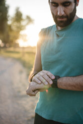 Sportsman looking at wristwatch while standing at park - CAVF27759