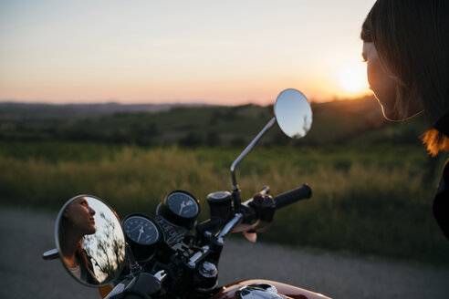 Nachdenkliche Motorradfahrerin, die auf ihrem Motorrad sitzend wegschaut - CAVF27775