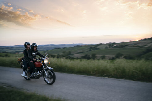 Junges Paar auf dem Motorrad auf der Landstraße bei Sonnenuntergang - CAVF27780