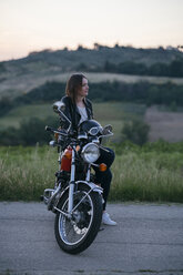 Thoughtful female biker sitting on motorcycle against landscape - CAVF27781