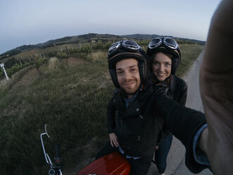 Hochformatiges Porträt eines glücklichen jungen Paares auf einem Motorrad - CAVF27782