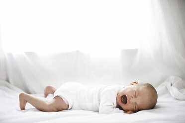 Side view of baby girl crying while lying on bed at home - CAVF27795