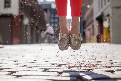 Low section of woman with confetti jumping on cobble street during sunny day - CAVF27827