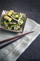 Close-up of cucumber salad and chopsticks on kitchen counter - CAVF27829