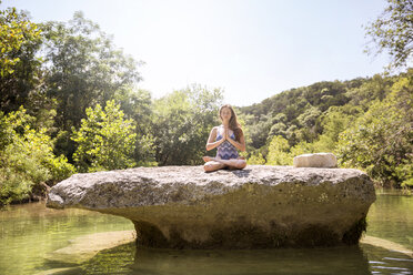 Teenager meditiert auf einem Felsen inmitten eines Sees im Wald - CAVF27884