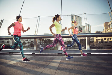 Side view of female athletes running on bridge in city - CAVF27894