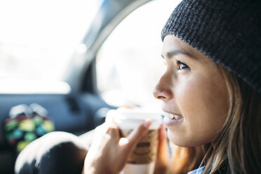 Nahaufnahme einer jungen Frau, die eine Kaffeetasse hält, während sie im Auto sitzt - CAVF27903