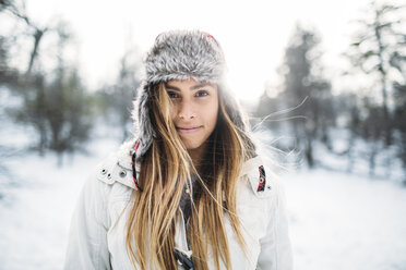 Portrait of smiling woman wearing fur hat at snow covered field - CAVF27918