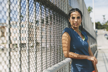 Portrait of sportswoman leaning on chainlink fence - CAVF27928