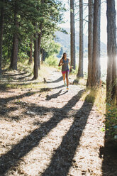 Frau läuft an Bäumen vorbei auf einem Weg an einem sonnigen Tag - CAVF27946
