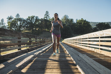 Sportswoman running at wooden bridge on sunny day - CAVF27951
