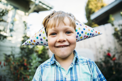 Porträt eines glücklichen Jungen mit Partyhut im Hinterhof, lizenzfreies Stockfoto