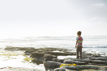 Rückansicht eines auf Felsen am Strand stehenden Jungen gegen den Himmel - CAVF27974