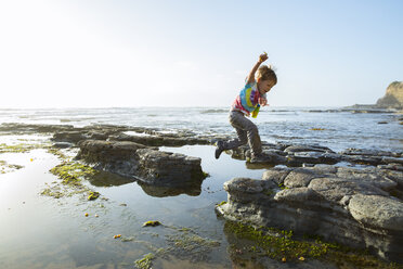 Seitenansicht eines Jungen, der am Strand gegen den klaren Himmel auf Felsen springt - CAVF27975