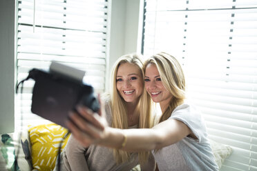 Smiling friends taking selfie while sitting on alcove window seat at home - CAVF27993