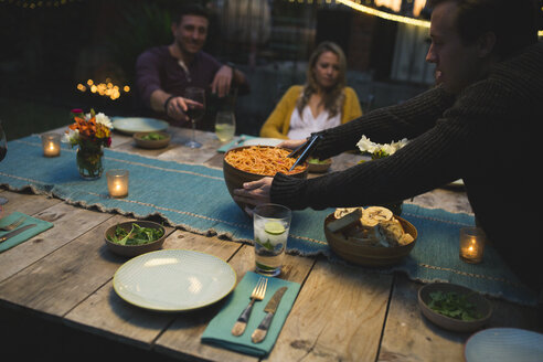 Mann hält Schüssel auf dem Tisch während des Abendessens mit Freunden auf der Terrasse - CAVF28009