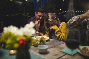 Happy couple sitting at table while enjoying dinner party with friends - CAVF28013