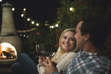 Couple with wineglasses sitting on sofa at patio - CAVF28020