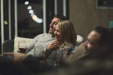 Smiling couple with friend sitting on sofa at patio - CAVF28021