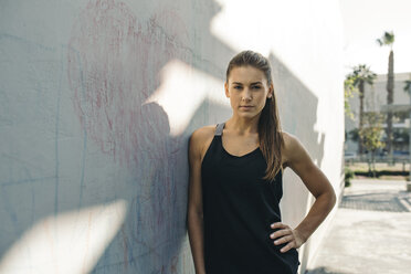 Portrait of confident female athlete leaning on wall outdoors - CAVF28047