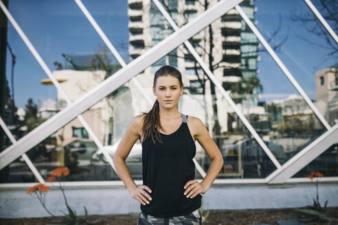 Porträt einer selbstbewussten Sportlerin, die mit den Händen auf der Hüfte in der Stadt steht - CAVF28051
