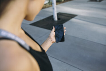 Cropped image of female athlete holding smart phone on footpath - CAVF28052