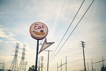 Low angle view of commercial sign and electricity pylons against sky - CAVF28109