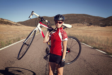 Porträt einer selbstbewussten Radfahrerin mit Fahrrad auf einer Landstraße - CAVF28122