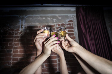 Ausgeschnittenes Bild von Freunden, die mit Tequila Shots gegen eine Backsteinmauer anstoßen - CAVF28127