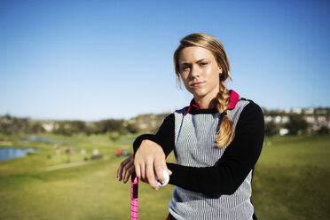 Portrait of confident female golfer standing on field against clear blue sky - CAVF28145