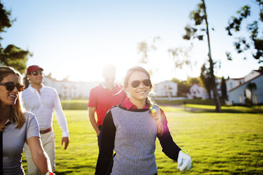 Happy male and female golfers walking on field during sunny day - CAVF28146