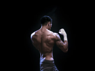Rückansicht eines männlichen Kickboxers, der vor einem schwarzen Hintergrund trainiert - CAVF28149