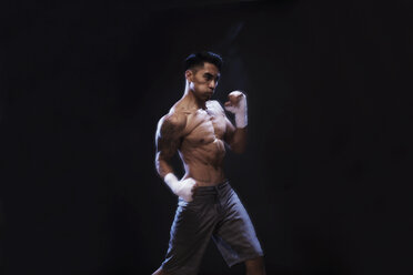 Determined kickboxer practicing against black background - CAVF28150