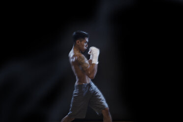 Seitenansicht eines männlichen Kickboxers, der gegen einen schwarzen Hintergrund kämpft - CAVF28152