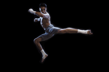 Männlicher Kickboxer in voller Länge, der in der Luft gegen einen schwarzen Hintergrund tritt - CAVF28153